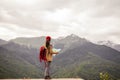 Man Traveler with map and red backpack searching location outdoor with rocky mountains on background
