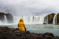 Tourist in a yellow jacket relaxing at the Godafoss waterfall in Iceland Royalty Free Stock Photo