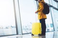 Tourist with yellow suitcase backpack is standing at airport on background large window, traveler man waiting in departure lounge Royalty Free Stock Photo