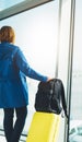 Tourist with yellow suitcase backpack is standing at airport on background large window, traveler woman waiting in departure loung Royalty Free Stock Photo