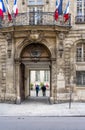 Tourists with backpacks are enjoying the architecture of the courtyard of the building with flags on the streets of old Paris