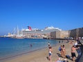 Tourists on the beach near rhodes town harbor with the cruise ship carnival vista moored behind the fort