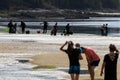 Tourists on a beach watching a group of shellfish gatherers prepare on the seashore to start shellfishing, with their buckets.