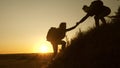 Tourists climb the mountain at sunset, holding hands. teamwork of business people. Traveler man holds out a woman`s hand