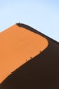 Tourists climb a red sand dune