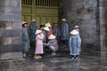 Tourists dressed in plastic raincoats and conical hats huddling together in stone porch, Hue Imperial City