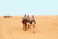 Tourists dressed in striped robes and orange turbans on their heads riding on two-humped camels for a walk Royalty Free Stock Photo