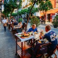 Tourists enjoy at restaurant terrace typically Spanish cuisine, seafood paella with squids, mussels, clams, and prawns