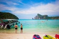 Tourists enjoy view on the Phi Phi island stayed on a sandy beach. Sunny day at the tropical island. Motor speed boat at the left