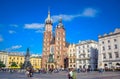 Tourists enjoying their time at Krakow`s Main Square with Adam Mickiewicz Monument and St. Mary`s Basilica, Poland