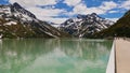 Tourists enjoying the view from Silvretta reservoir dam, Montafon, Austria with snow-capped mountains in the background.