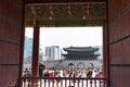 Tourists at Gyeongbokgung palace. Picture taken from the inside through a large door. Wooden red gate. Modern buildings at the Royalty Free Stock Photo
