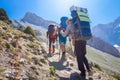 Tourists hiking in mountains with backpacks on sunny summer day. Hikers on mountain trail. Trekking in Fann mountains, Tajikistan