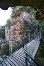 Tourists hiking at steep zigzag trail of Grand Stairway along red rock shear cliff with vegetation in Blue Mountains National Park