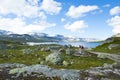 Tourists hiking towards dam of Lake Finsevatnet, snowy mountains and glacier Hardangerjokulen in Finse, Norway Royalty Free Stock Photo