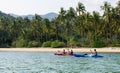 Tourists kayaking on sunny tropical beach with palm trees