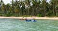 Tourists kayaking on sunny tropical beach with palm trees