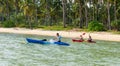 Tourists kayaking on sunny tropical beach with palm trees