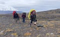 Tourists with large backpacks and trekking poles walk along the autumn tundra