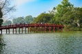 Tourists and locals crossing traditional Oriental style red Huc Bridge over Hoan Kiem Lake in Hanoi