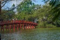 Tourists and locals crossing traditional Oriental style red Huc Bridge over Hoan Kiem Lake in Hanoi