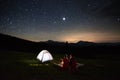 Tourists near campfire and tent under night starry sky Royalty Free Stock Photo