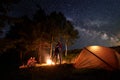 Tourists during night of camping around campfire near tent under starry sky on background of trees