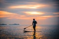 Tourists paddle surfboards in the sunset on a day when the sea has little waves