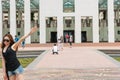 Tourists posing and walking in in front of Australian Parliament building with woman blurred as she walks out of bottom of frame