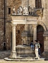 Tourists posing at The well of Griffins and Lions in the big square of Montepulciano, Italy.