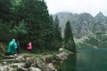 Tourists in raincoats walk in the rain along a rock path along the shore of a mountain lake. Hiking by the lake on the trail on Royalty Free Stock Photo