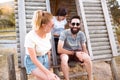 Tourists relaxing. Group of three friends sitting on wooden camp stairs enjoying and laughing in the countryside. Camp adventure