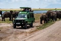 Tourists in safari jeeps watching and taking photos of big wild elephant crossing dirt road in Amboseli national park Royalty Free Stock Photo
