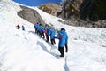 Tourists in single file ascending icy slope at glacier exploration