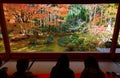 Tourists sit on the tatami floor of a tea room & enjoy the beautiful view of a Japanese courtyard garden