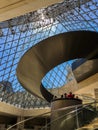 Tourists and spiral staircase inside glass pyramid in Louvre, Paris, France