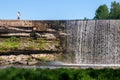 Tourists stand on the edge of Jagala waterfall on a cliff of limestone against the sky.