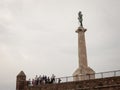 Tourists standing in crowd in front of Victor statue on Kalemegdan fortress, seen from the bottom.