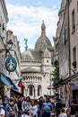 Tourists stroll in Montmartre near Basilica Sacre Coeur designed by Paul Abadie, 1914 - a Roman Catholic Church and minor