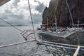 Tourists on traditional Philippino fisherman boats crossing the waters near grey limestone cliffs on a cloudy day of El Nido at Royalty Free Stock Photo