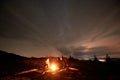 Tourists travelers sitting by burning campfire on mountain valley under starry cloudy sky. Royalty Free Stock Photo