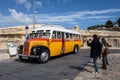 Tourists in Valletta, Malta, taking photos of a vintage orange maltese bus parked in downtown street. Royalty Free Stock Photo