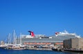 Tourists walk along the seafront at rhodes town harbor with the cruise ship carnival vista moored near sailing boats