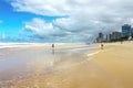 Tourists walk along wet beach by turbulent Pacific Ocean under stormy skies with tall towers of Surfers Paradise - Gold Coast Quee Royalty Free Stock Photo