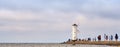 Tourists walk on the pier to a lighthouse on the Baltic Sea in Swinoujscie in Poland. With blurred cloudy sky in the background