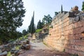 Tourists walking through and taking pictures of ruins at ancient Delphi Greece with walls and stairs and trees