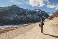 Tourists walk to black mountain with snow on the top and brown mountain with Houses and glacial trace on yellow stone ground.