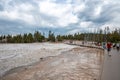 Tourists walking on wooden pathway amidst geothermal landscape at geyser basin