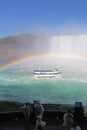 Tourists watch Niagara Falls tour boat under a full rainbow vert