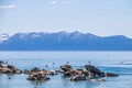 Tourists in water on paddleboards and climbing on rocks in blue Lake Tahoe with snow tipped mountains in distance Royalty Free Stock Photo